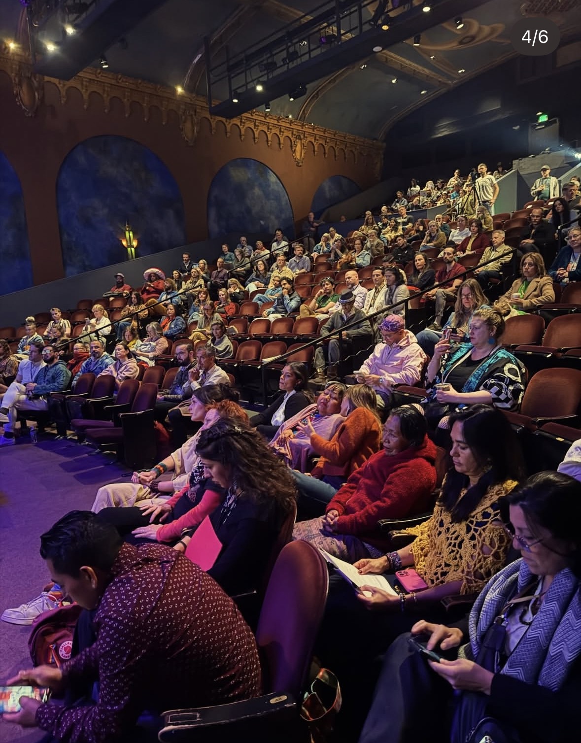 A full audience seated under the Brava Theater's painted arches during a Psychedelic Culture 2026 session.